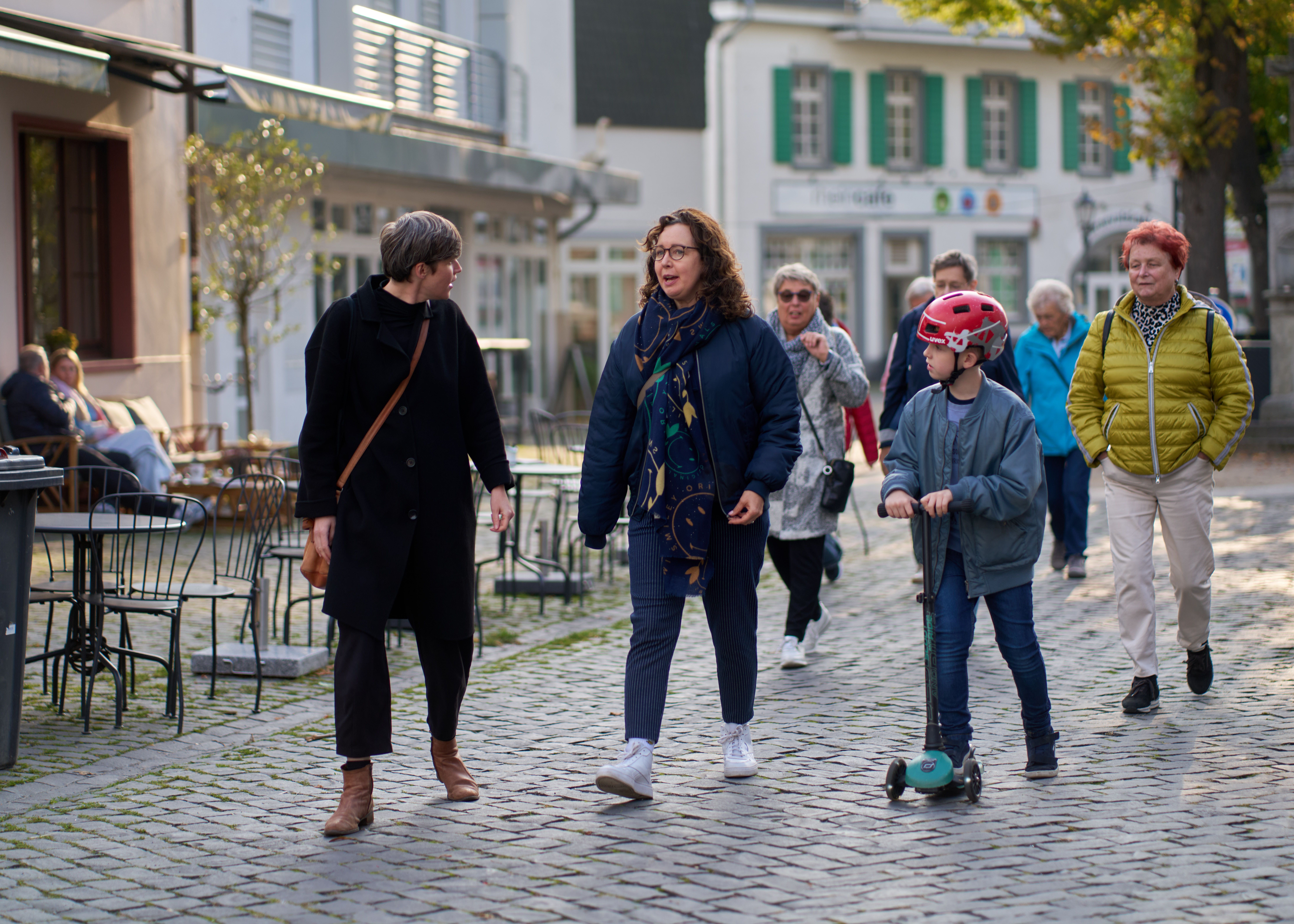 Mehrere Menschen laufen durch die Stadt. Eine Person erzählt den anderen etwas.